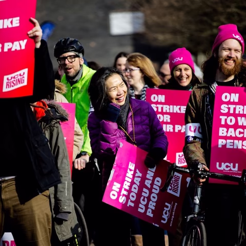 Photograph of people holding signs reading: On Strike Today with central figure smiling.