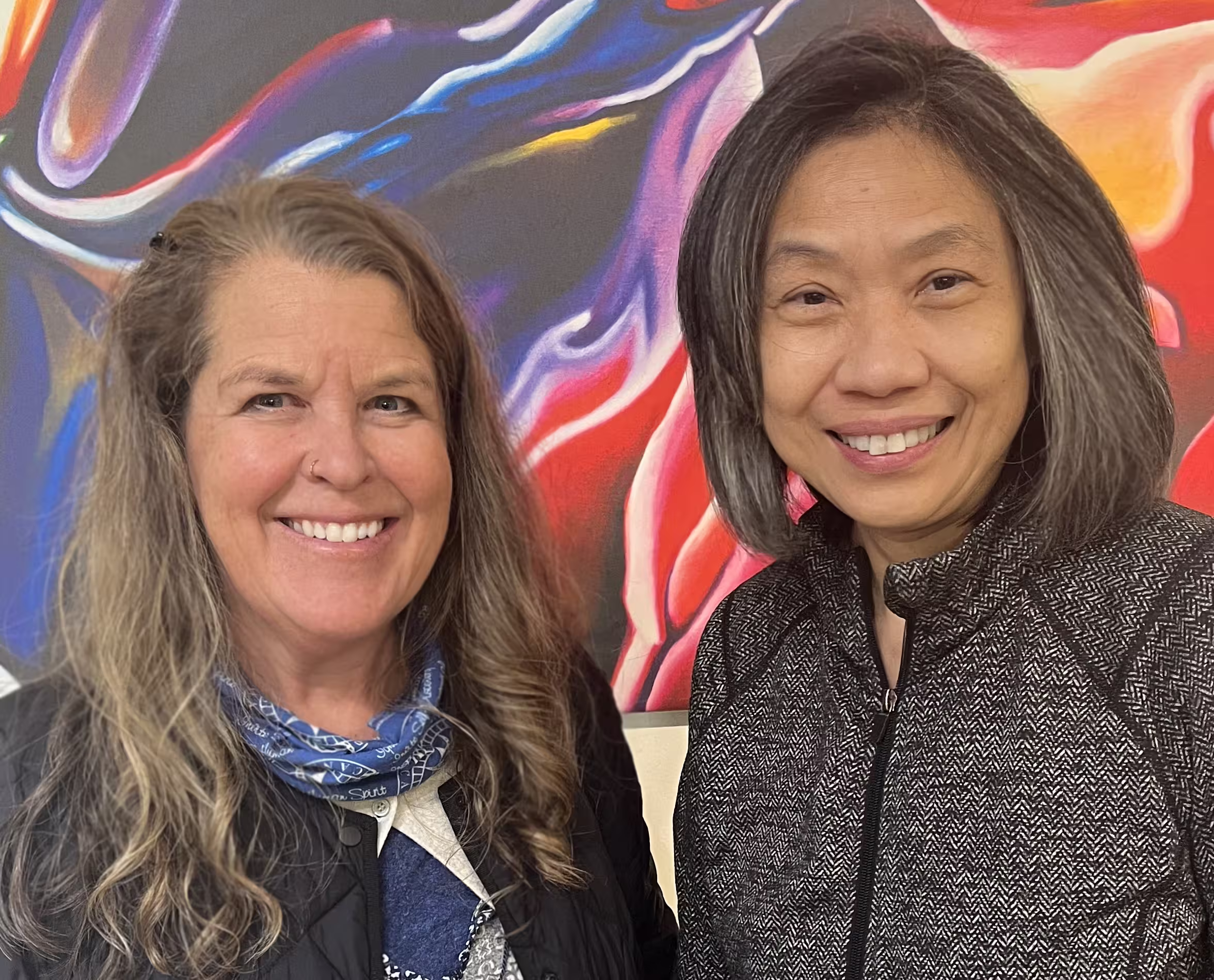 Colour photo of two people smiling in front of a colourful abstarct artwork.